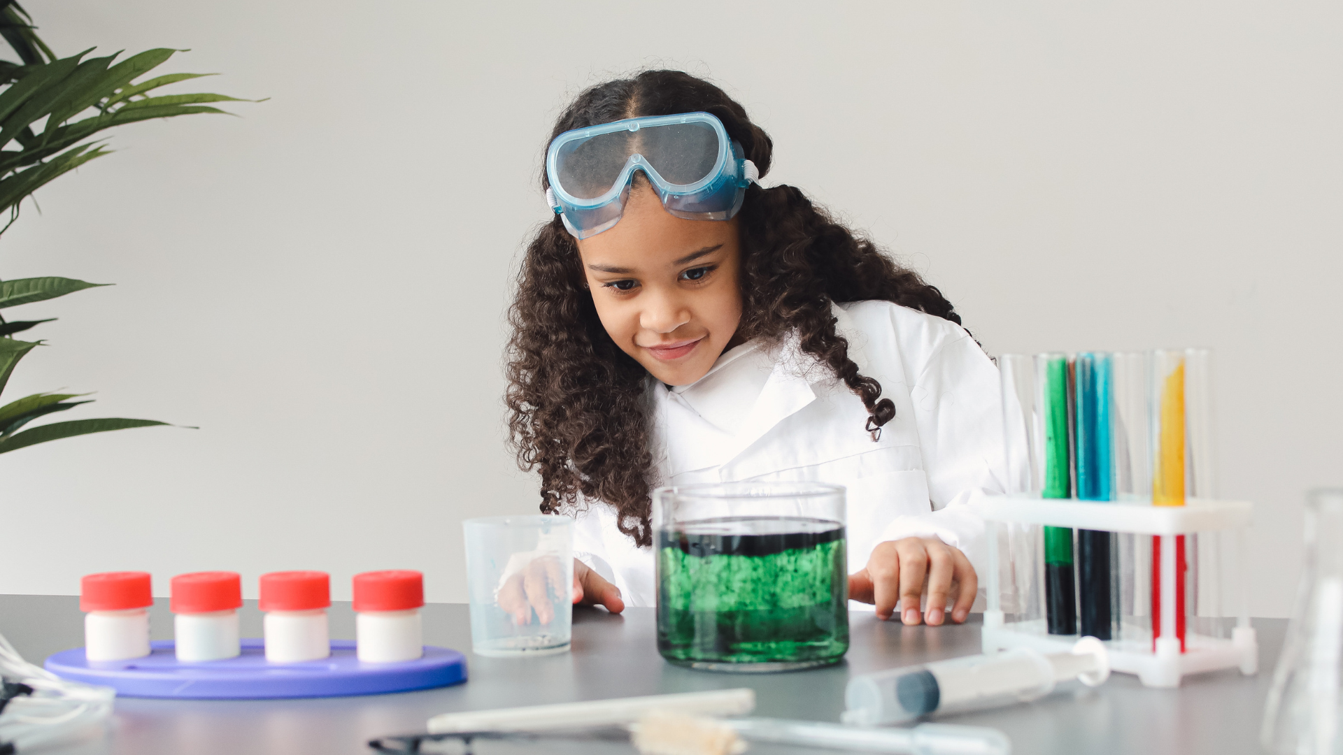 photographie d'une petite fille déguisée en scientifique avec une blouse blanche et de lunettes, qui mène une expérience scientifique avec des tubes à essais contenant des liquides colorés