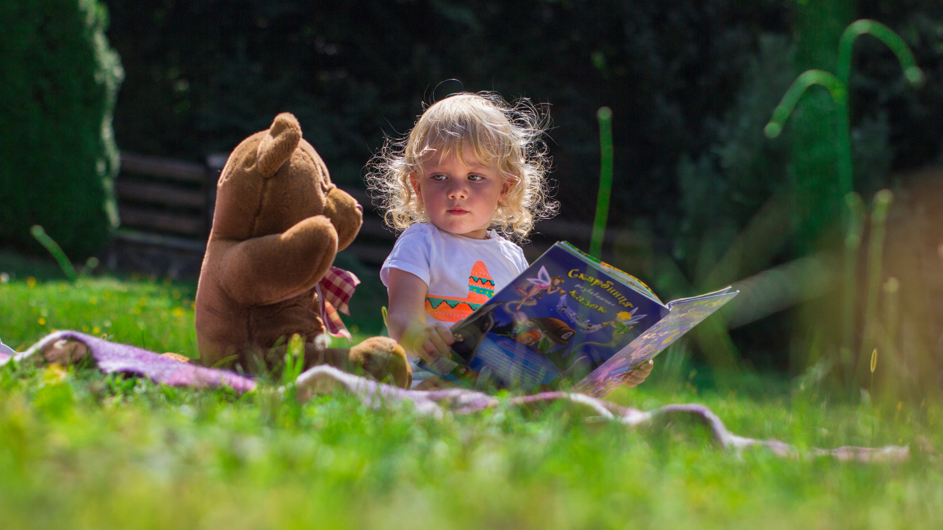 un enfant qui lit à un ours en peluche dans un jardin